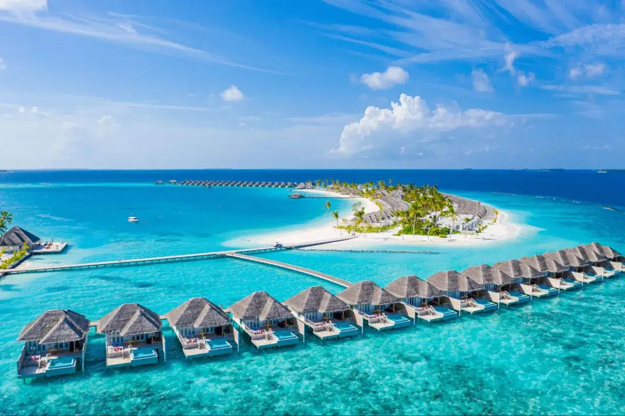 Bungalows sobre el agua en un resort de Maldivas, con aguas turquesas y una isla tropical. &iexcl;Un sue&ntilde;o de Maldivas low cost!