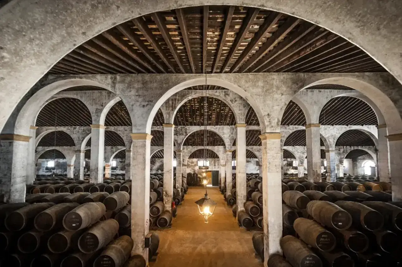 Bodega en Jerez de la Frontera, con hileras de barricas de roble bajo arcos de piedra. Un lugar imprescindible que ver en Jerez de la Frontera en un d&iacute;a.