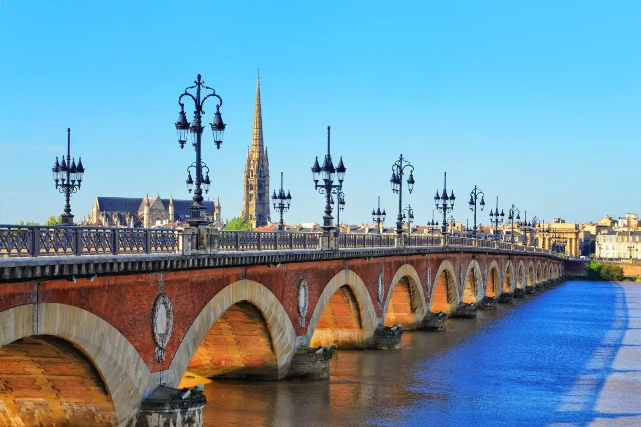 Puente de piedra con farolas y la silueta de la catedral, un cl&aacute;sico que ver en Burdeos.