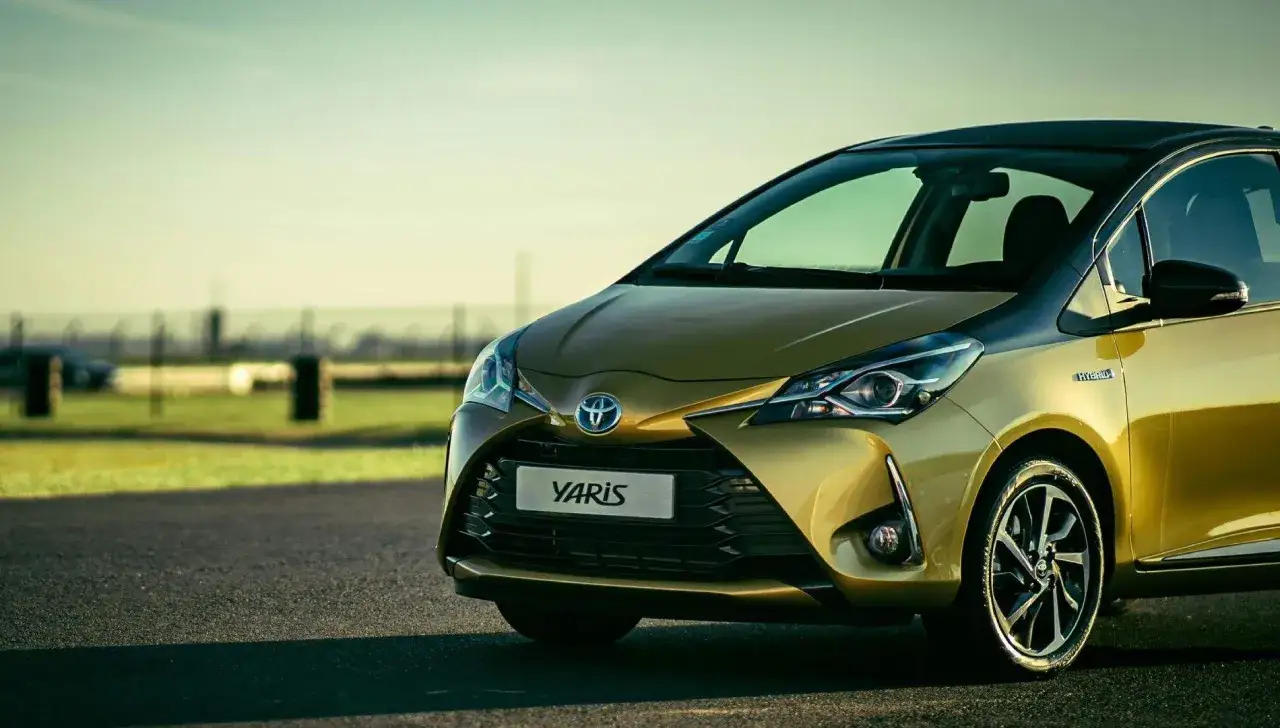 Un Toyota Yaris dorado, uno de los coches mas fiables de segunda mano, aparcado en una carretera con un fondo difuminado.