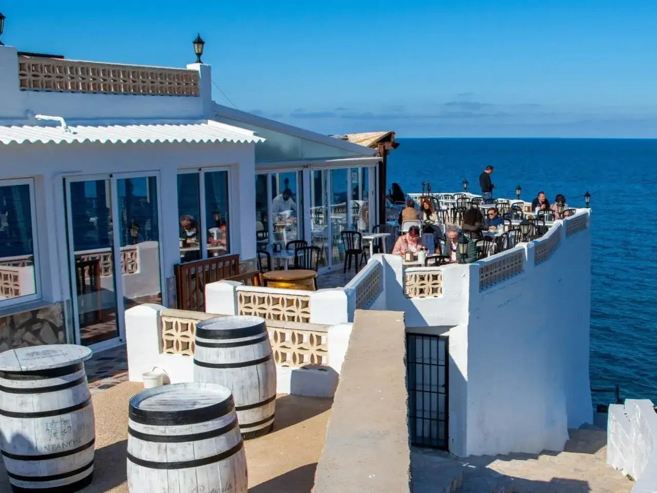 Terraza con vistas al mar, ideal para saber donde comer en Denia. Gente disfrutando en mesas al aire libre.