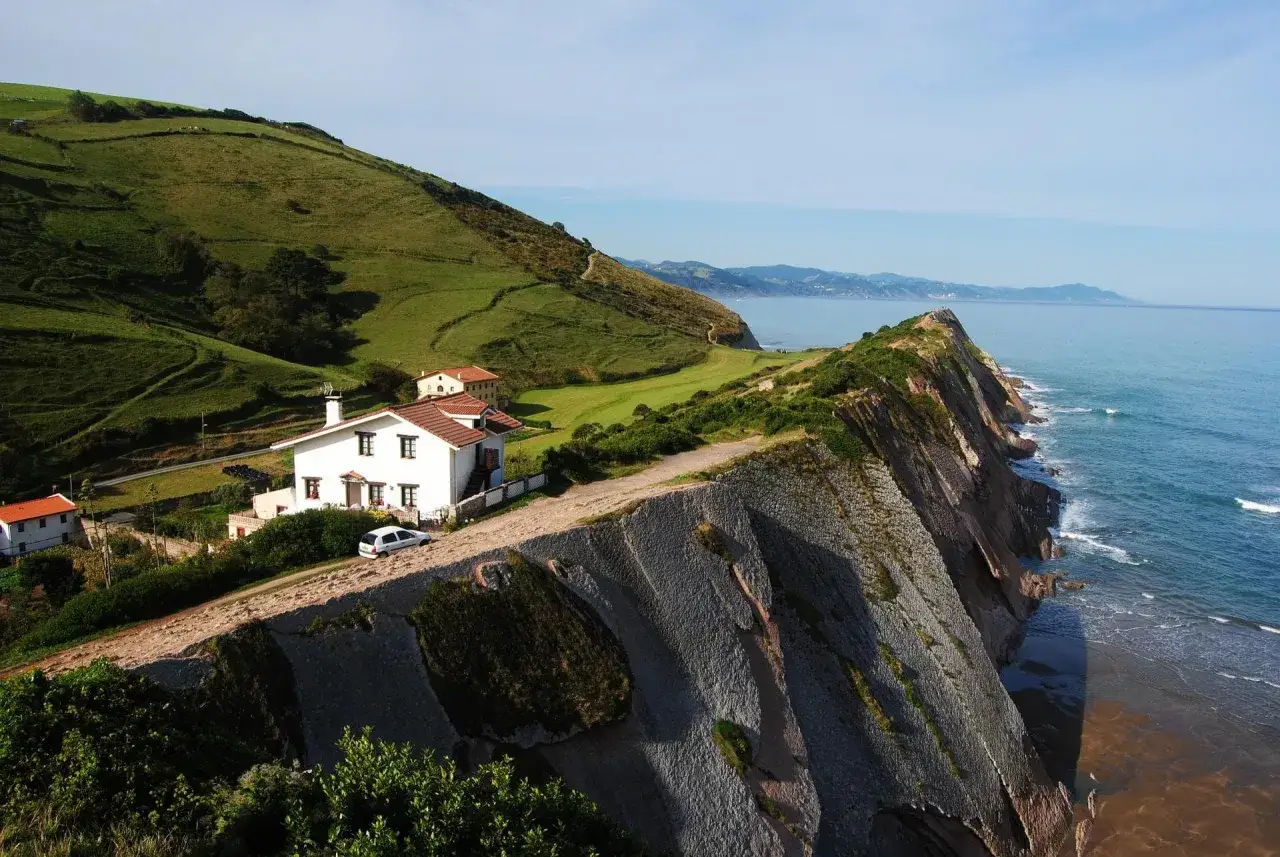 Casas blancas en acantilado verde, ideal para un viaje de Pa&iacute;s Vasco en 5 d&iacute;as. El mar azul y la costa escarpada crean un paisaje impresionante.