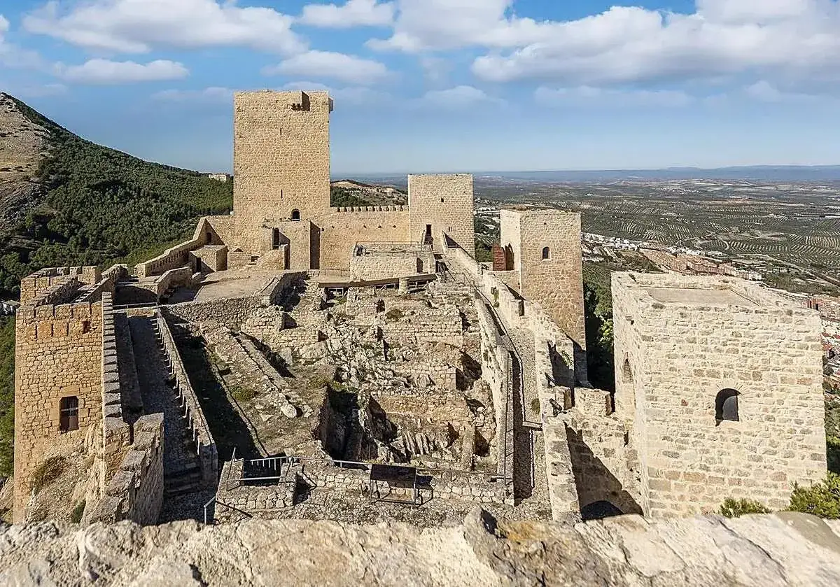 Impresionante castillo de piedra en lo alto de una colina, con vistas a un paisaje de olivos. Un lugar imprescindible que ver en Ja&eacute;n.