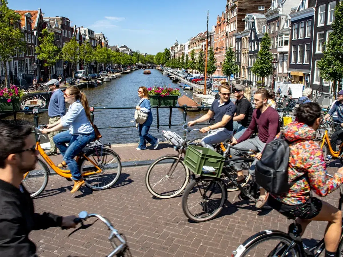 Gente en bicicleta por un canal de &Aacute;msterdam, un consejo para viajar a &Aacute;msterdam es disfrutar de su ambiente ciclista.