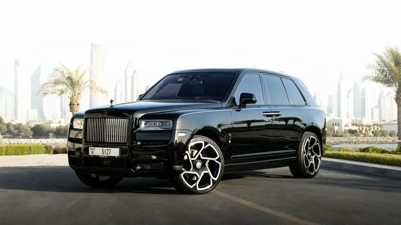 Un Rolls-Royce negro reluciente, perfecto para viajar a Dub&aacute;i, con palmeras y rascacielos de fondo.