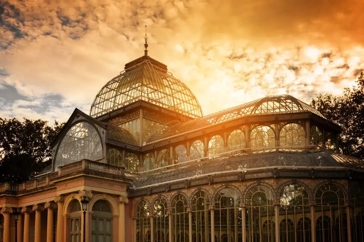 Palacio de Cristal en el Retiro, un lugar imprescindible que ver en Madrid, ba&ntilde;ado por la luz dorada del atardecer.
