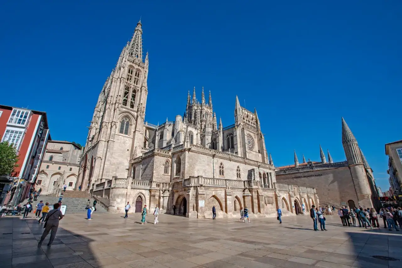La Catedral de Burgos, un imprescindible que ver en Burgos, se alza majestuosa bajo un cielo azul. Turistas pasean por la plaza.