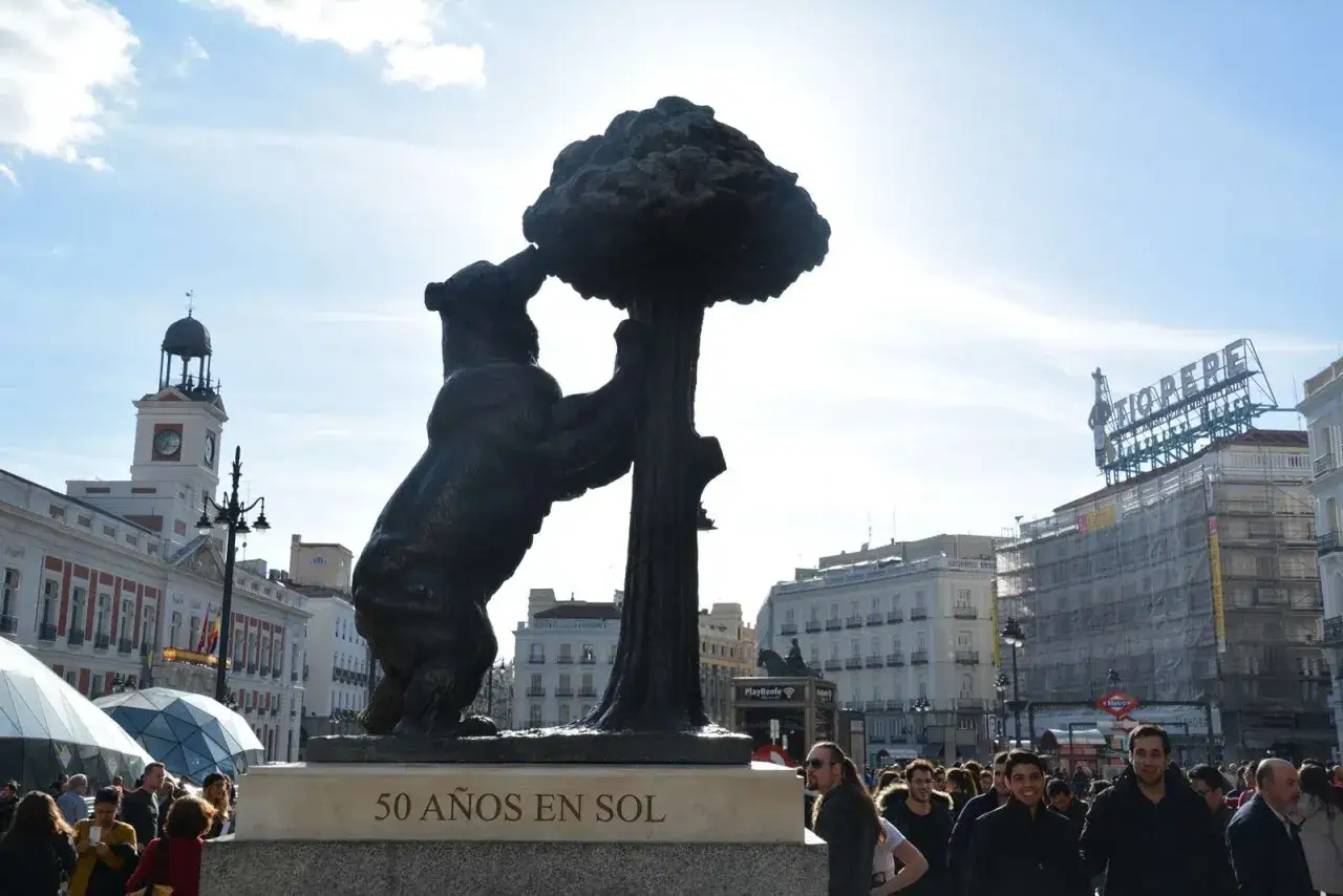 El Oso y el Madro&ntilde;o, un s&iacute;mbolo de Madrid en un d&iacute;a soleado. Gente pasea por la plaza.