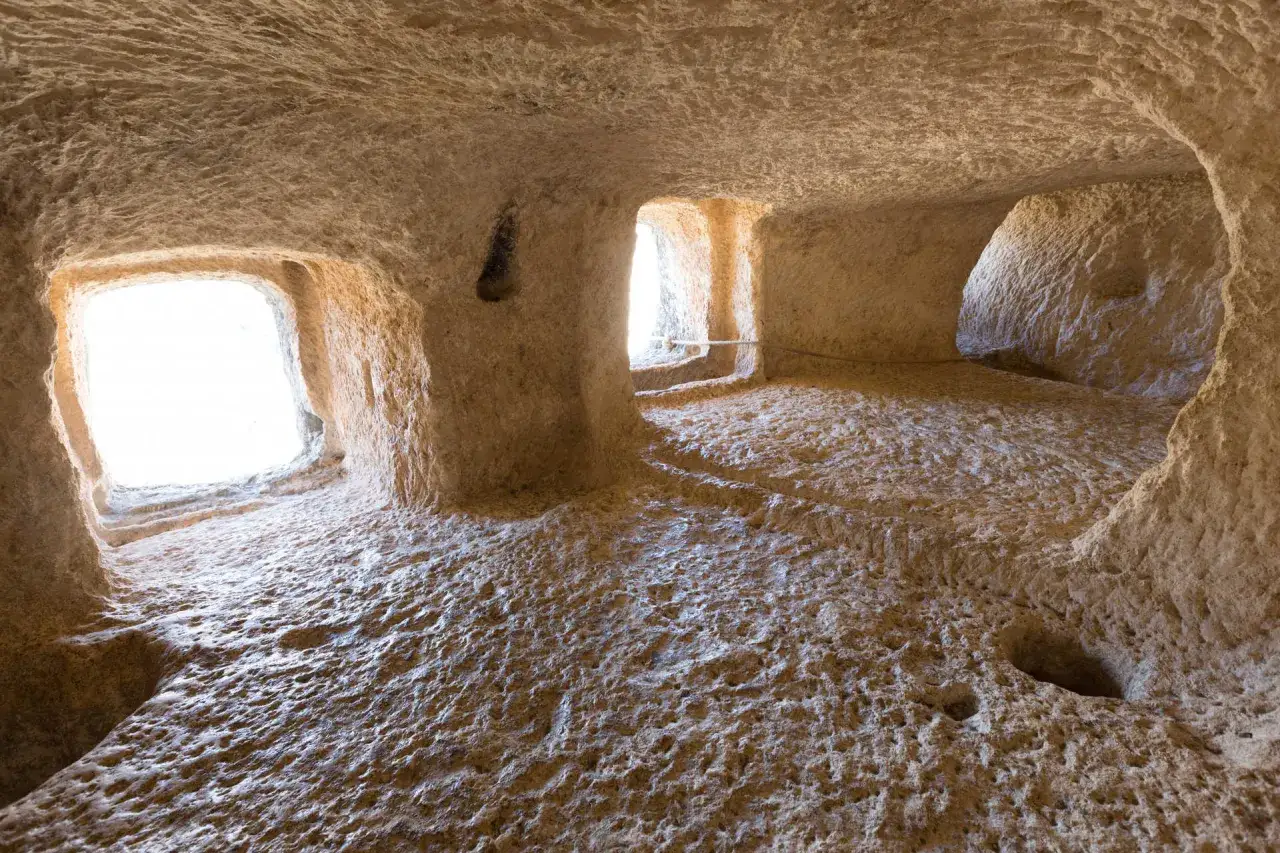 Interior de cuevas en Bocairent que ver. Luz natural ilumina el suelo rugoso y las paredes excavadas.