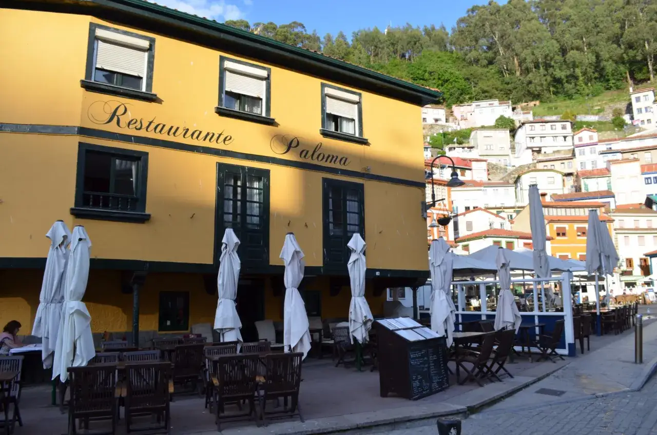 Restaurante Paloma, un lugar ideal donde comer en Cudillero. Mesas y sillas de madera esperan en su terraza, bajo el sol asturiano.