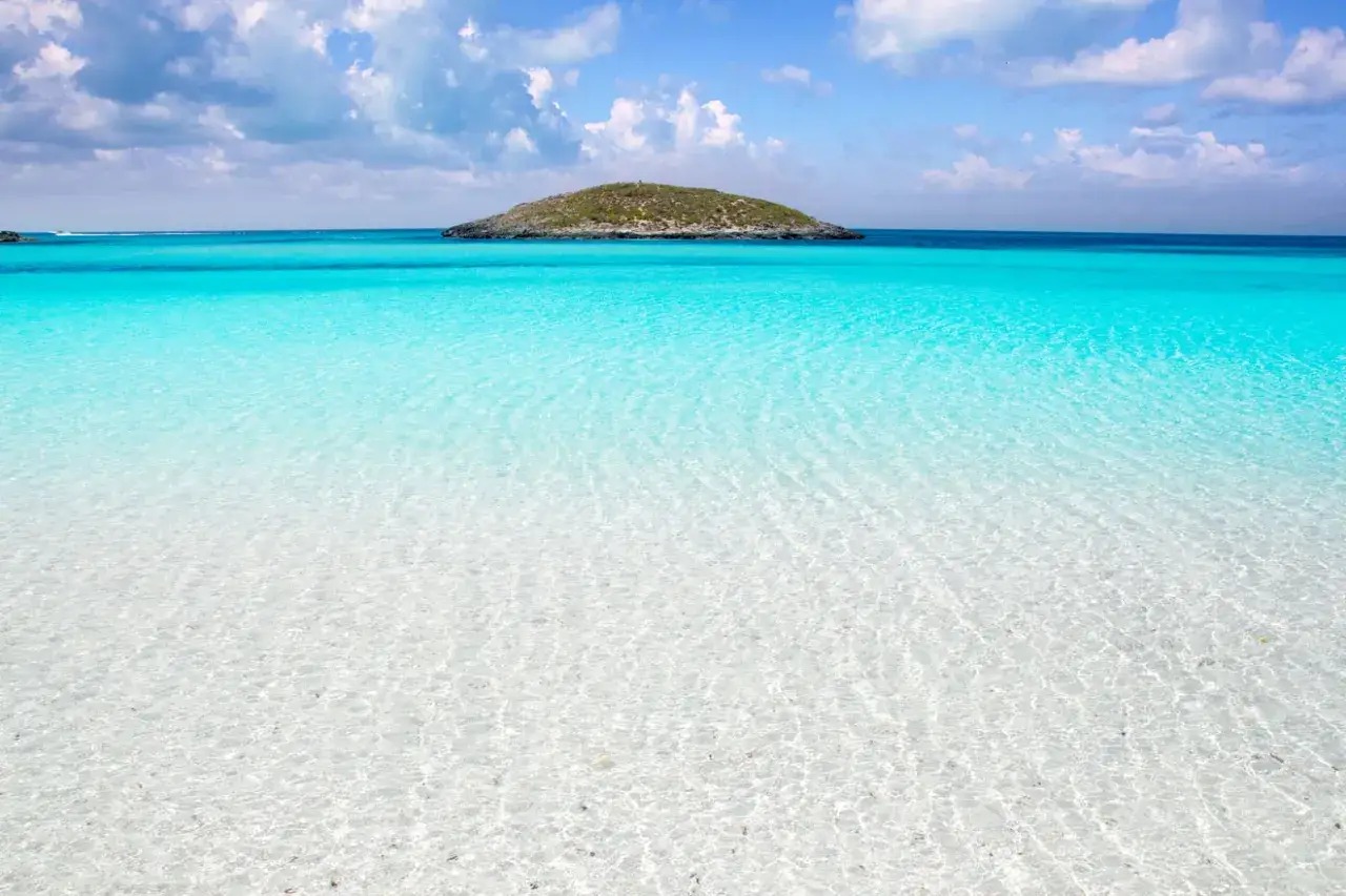 Aguas turquesas y arena blanca en Formentera. Un para&iacute;so para descubrir qu&eacute; ver en Formentera, con una peque&ntilde;a isla al fondo.