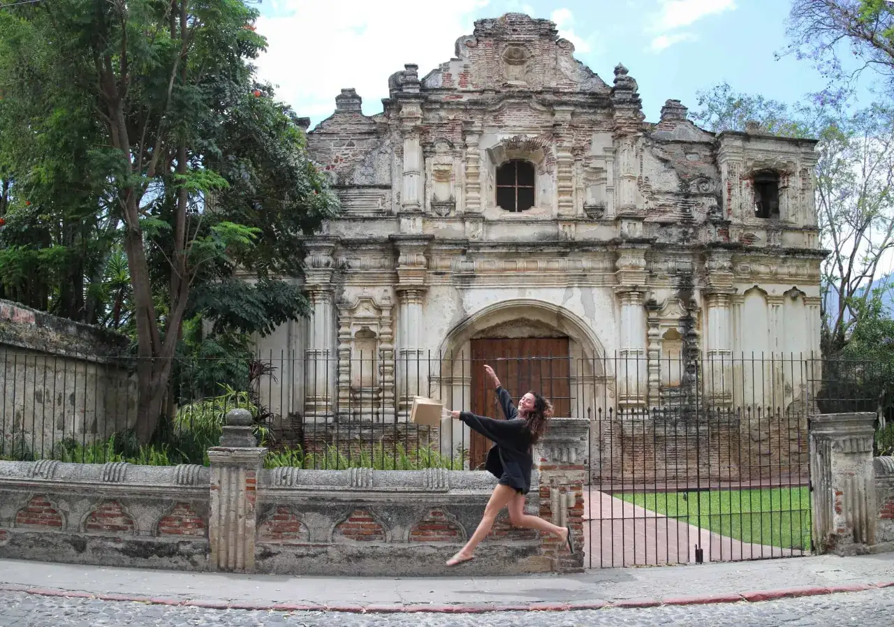 Una joven salta de alegr&iacute;a frente a las ruinas de una iglesia colonial, un sitio imperdible que ver en Antigua Guatemala.