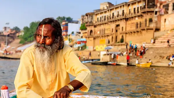 Un hombre con barba y marca en la frente navega en el Ganges, una escena típica al viajar a la India.