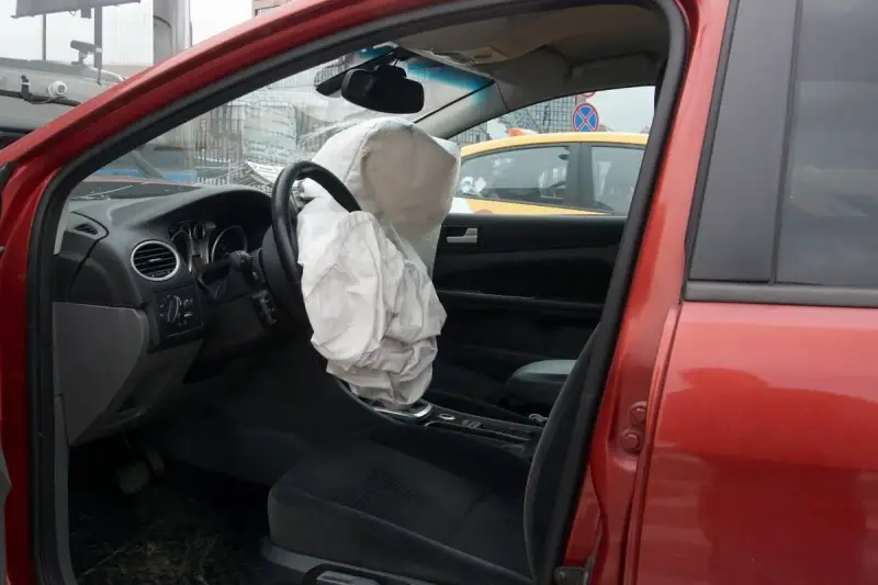 Interior de coche rojo con airbag del conductor desplegado, indicando la dirección del vehículo activa o pasiva tras un impacto.