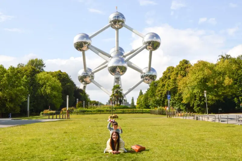Familia posa frente al Atomium, un icono de que ver en Bruselas. Un niño salta detrás de su madre en el césped.