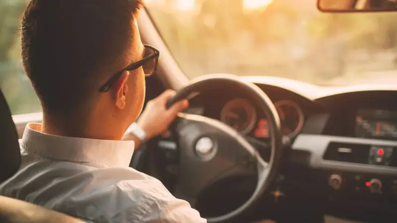 Hombre con gafas de sol conduce al atardecer. ¡Cuidado con la velocidad, te pueden multar!