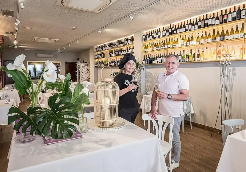 Pareja sonriente en un restaurante con estanterías llenas de vino. Un lugar ideal para saber donde comer en Logroño.